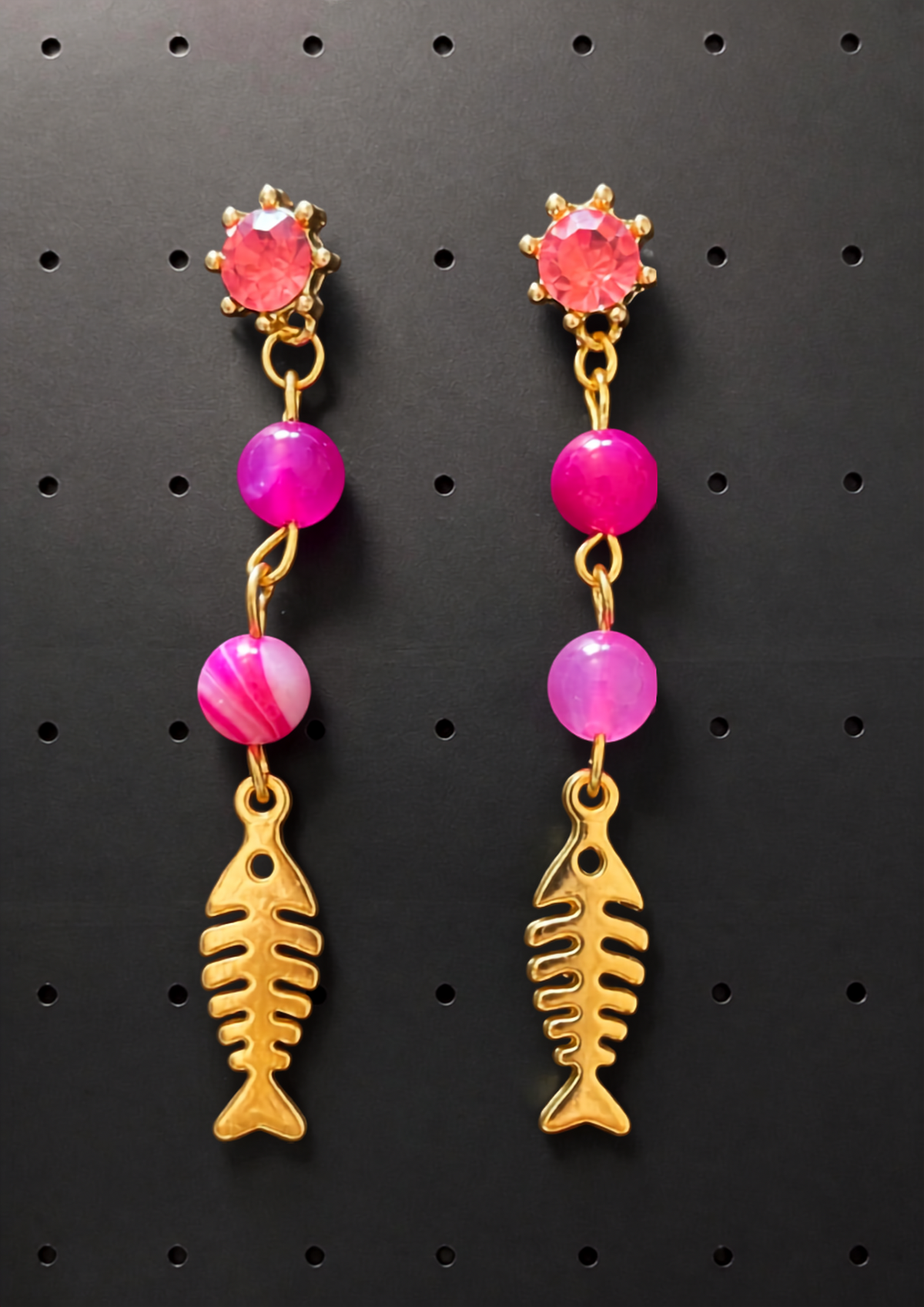 Boucles d'oreilles pendantes avec perles d'agate rose fuchsia et charm arête de poisson en métal doré sur fond noir